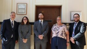 Donald Gibson, Amy Xedis, Vinny Flood, Lisa Smith, & Daniel Byas standing in front of wooden door.